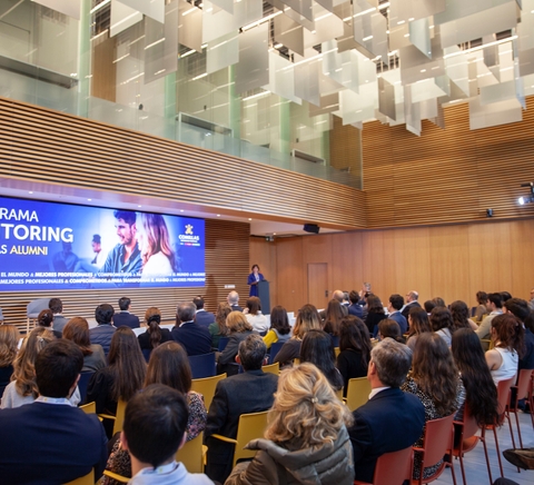 Imagen de un evento de mentoring con un ponente frente a una audiencia en un auditorio moderno.