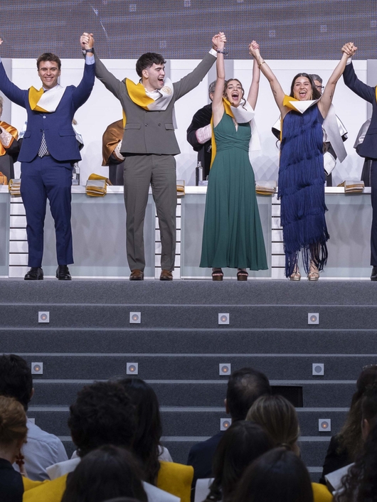 Un grupo de graduados se celebra en una ceremonia sosteniendo las manos en alto.