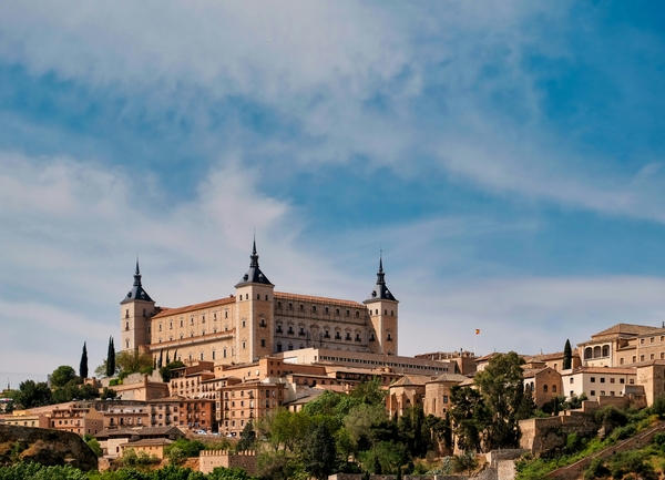 Una vista panorámica de un castillo rodeado de edificaciones y vegetación bajo un cielo azul.