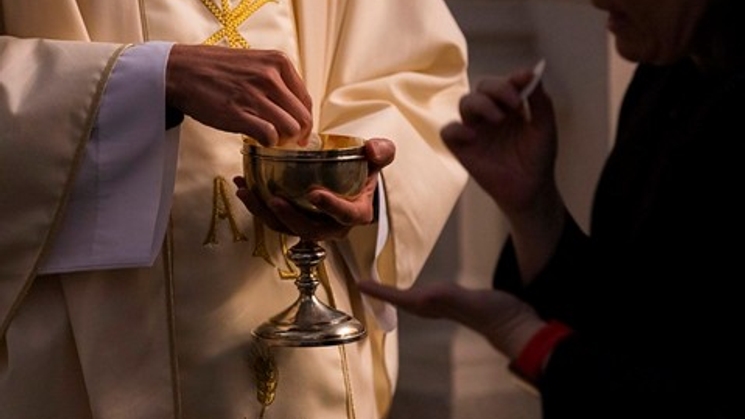 Un sacerdote con vestiduras litúrgicas sostiene un cáliz mientras una persona extiende la mano.