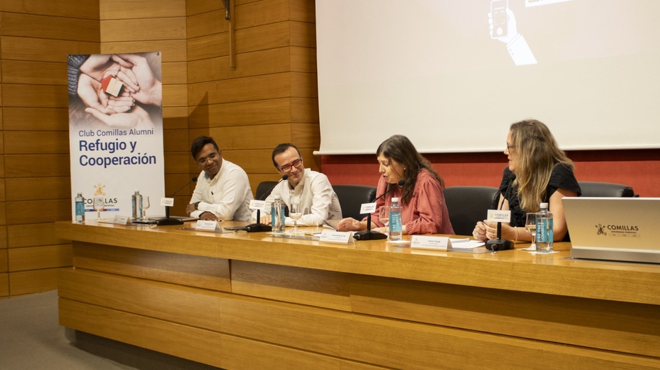 Four individuals sitting at a panel discussion in a conference room with a banner about refuge and cooperation.