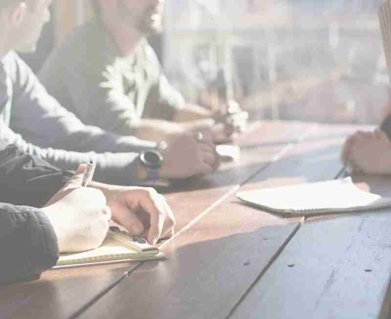 Un grupo de personas colaborando y escribiendo en una mesa de trabajo.