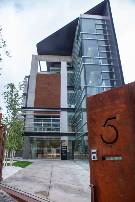 Modern multi-story building featuring a mix of glass and wood panels, with a large, rusty metallic sculpture exhibiting the number 5 in the foreground.