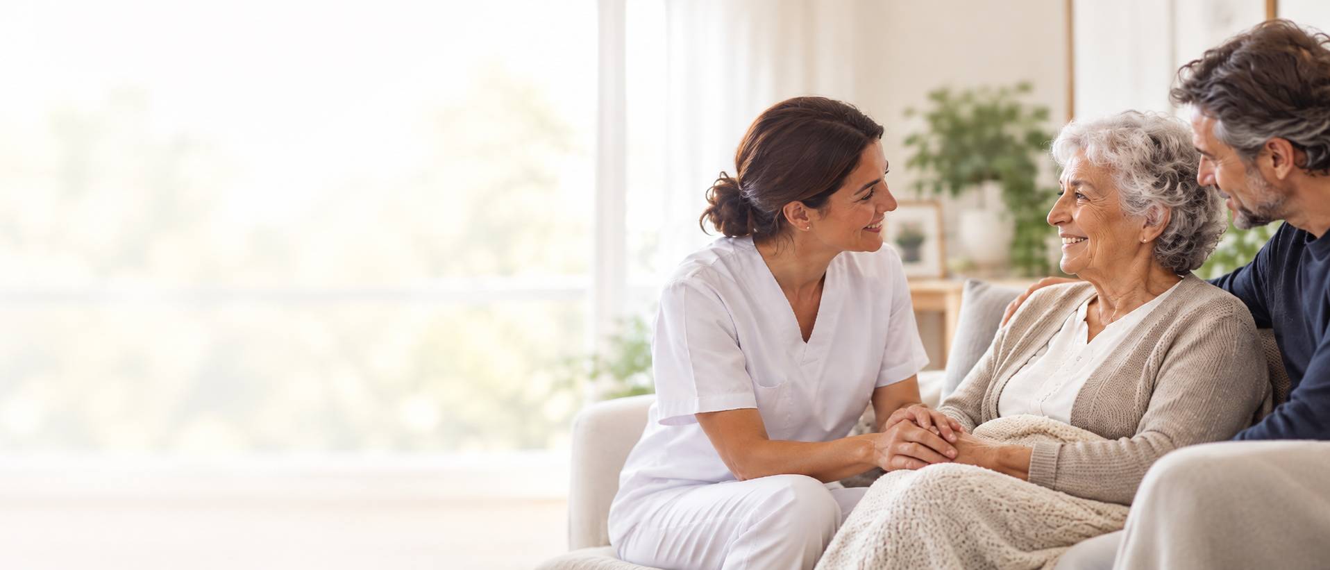 Una enfermera sonriente conversa con una anciana y un familiar en un ambiente acogedor.