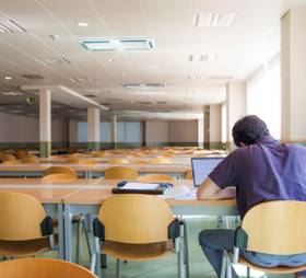 A person working alone in a large, empty lecture hall with rows of desks and chairs.