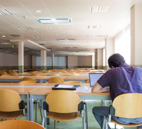 A person working alone in a large, empty lecture hall with rows of desks and chairs.