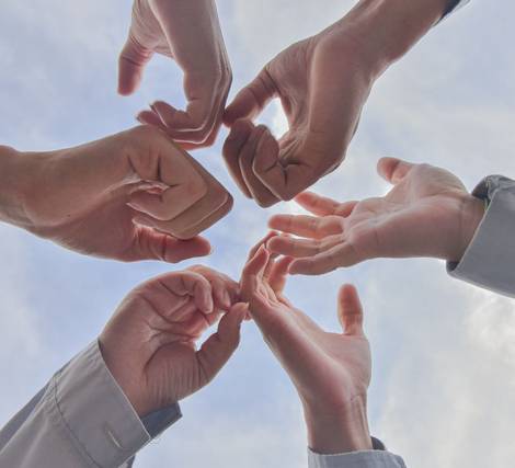 Multiple hands forming a circle against a sky background