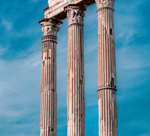 La imagen muestra tres columnas clásicas de un antiguo templo contra un cielo azul.