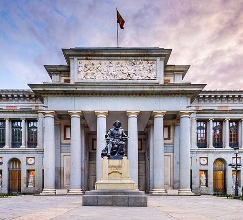 La imagen muestra la fachada del Museo del Prado en Madrid, destacando su arquitectura neoclásica y la estatua de un artista en primer plano.