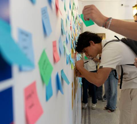Un grupo de personas está interactuando con una pared llena de notas adhesivas de colores.