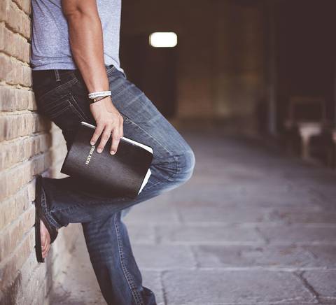 Un hombre apoyado en una pared de ladrillos con un libro en la mano.