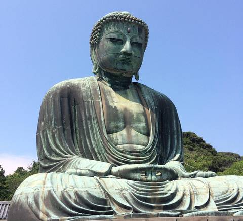 Una estatua de Buda de gran tamaño en posición de meditación frente a un cielo azul.