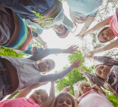 Un grupo de niños sonriendo mientras hacen una foto en círculo, con los brazos extendidos hacia el centro.
