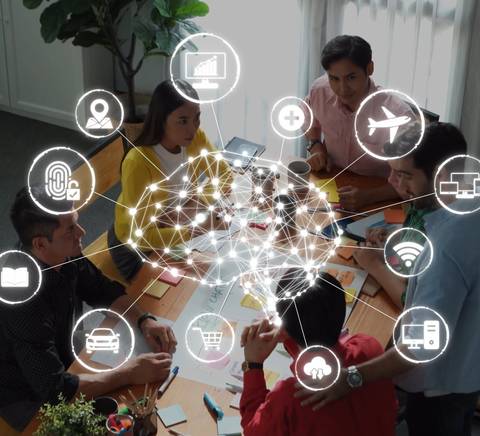 Un grupo de personas discutiendo ideas alrededor de una mesa con elementos visuales relacionados con la tecnología y la conectividad.