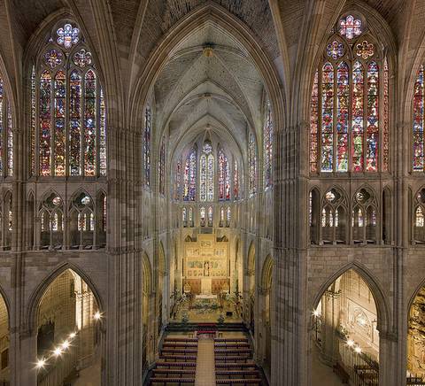 Interior de una catedral gótica con vitrales coloridos y altares elaborados.