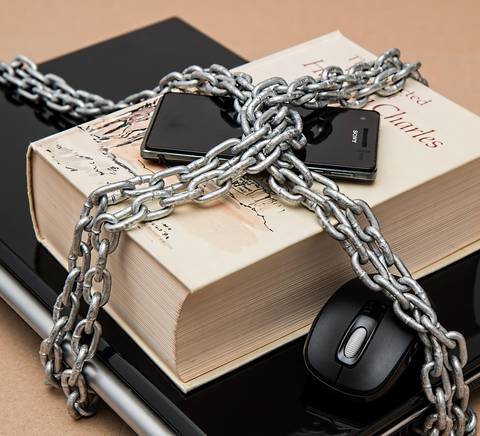 Una cadena gruesa envuelve un libro y varios dispositivos electrónicos sobre una superficie oscura.