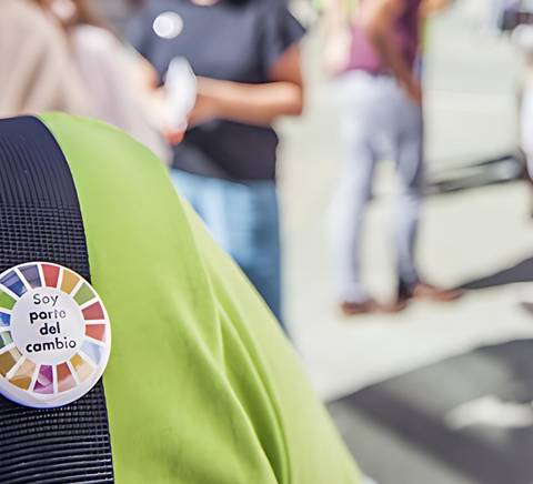 A close-up of a badge reading 'Soy parte del cambio' pinned on a person's shirt in a bustling office environment.