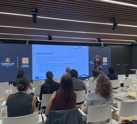 Una presentación en un salón con varias personas sentadas y un ponente hablando frente a una pantalla.