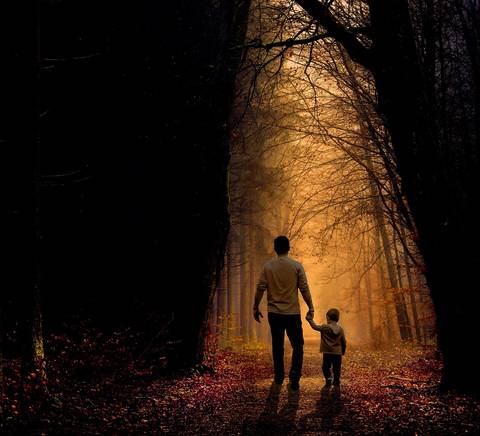 Una figura adulta y un niño caminan de la mano por un sendero iluminado entre árboles oscurecidos.