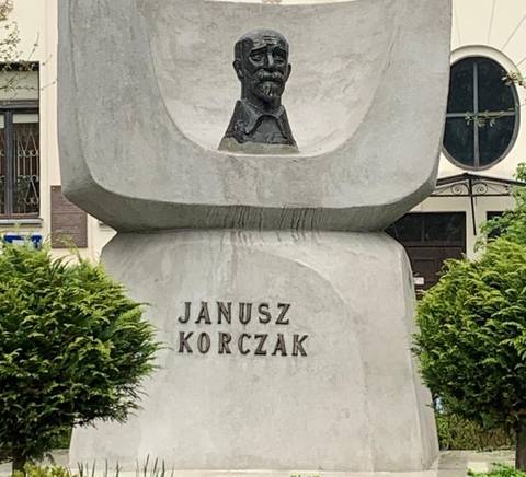 La imagen muestra un monumento en honor a Janusz Korczak con un busto y una base de concreto.