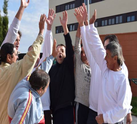 A group of elderly people excitedly raising their hands together in a celebratory gesture outdoors.