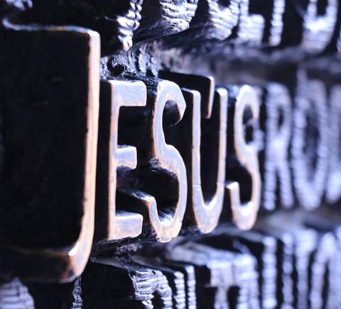 Imagen en primer plano de la palabra 'Jesús' tallada en un material oscuro.