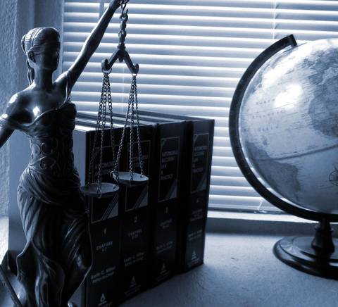 Una figura de la justicia sostiene balanzas junto a una esfera terráquea y libros en un ambiente iluminado.