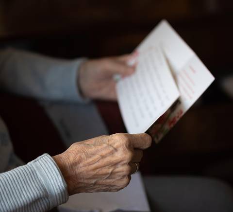 Una persona mayor sostiene una carta con ambas manos mientras la lee.