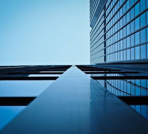 Vista desde abajo de un edificio moderno con ventanas reflejantes bajo un cielo azul.