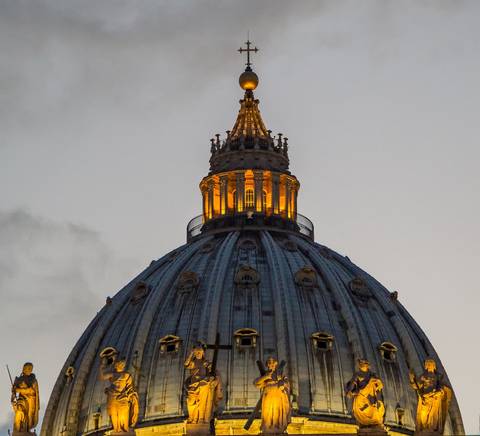 La imagen muestra la cúpula de la Basílica de San Pedro iluminada al atardecer.