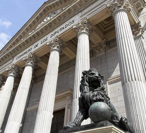 La imagen muestra la fachada del Congreso de los Diputados en Madrid, destacando una escultura de un león en primer plano.