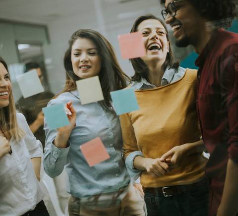 Un grupo de cuatro personas sonríen y conversan frente a una pared con notas adhesivas de diferentes colores.