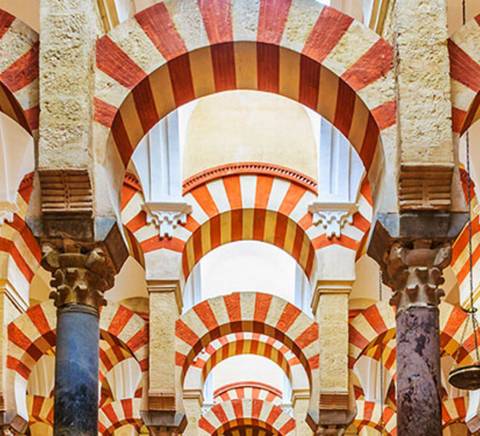 La imagen muestra un interior arquitectónico con arcos de colores rojo y blanco, típicos de la tradición islámica en España.