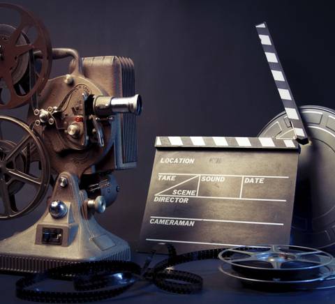 Una antigua cámara de cine con un claquet y rollos de película en un fondo oscuro.
