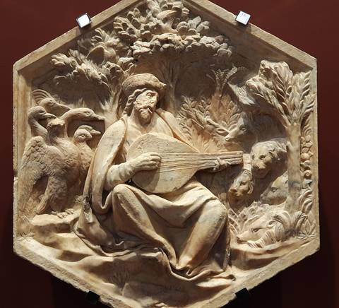 Un relieve en madera que representa a un hombre tocando laúd rodeado de naturaleza.