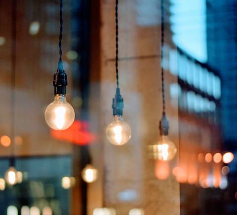 La imagen muestra bombillas colgantes iluminando un ambiente urbano reflejado en una ventana.