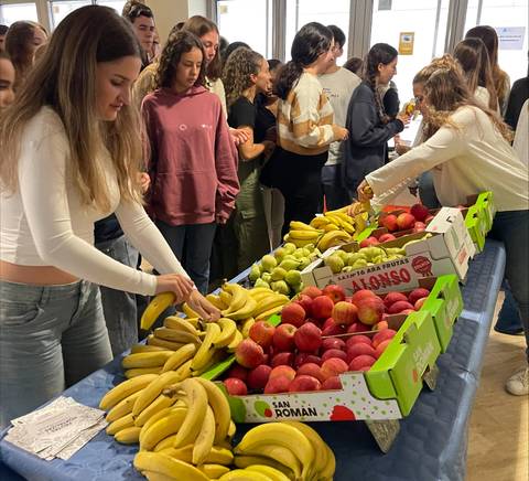 Un grupo de personas elige frutas en una mesa llena de bananas, manzanas y peras.