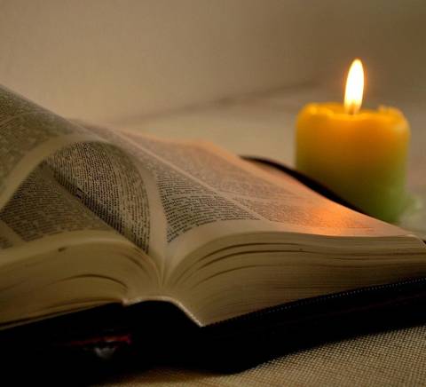 Un libro abierto junto a una vela encendida que crea un ambiente acogedor.