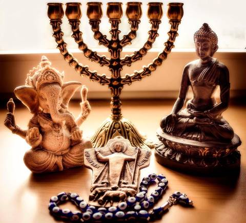La imagen muestra una reunión de diversas figuras religiosas, incluyendo a Ganesh, Buda, una menorá y un crucifijo, rodeadas de un collar de ojos turcos.