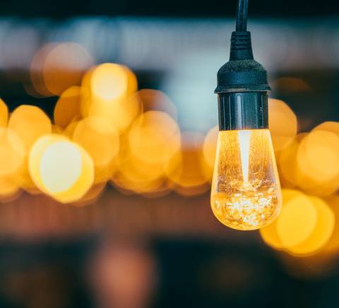 Una bombilla encendida con fondo desenfocado de luces cálidas.