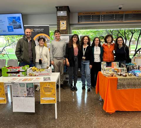 A group of people standing behind a table displaying various food items at an indoor event.