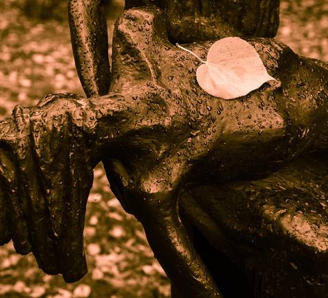 Una escultura de metal con una hoja sobre ella, rodeada de un ambiente otoñal.
