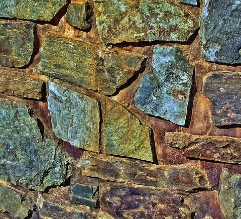 Una pared de piedra compuesta por diversas losas de diferentes colores y texturas.