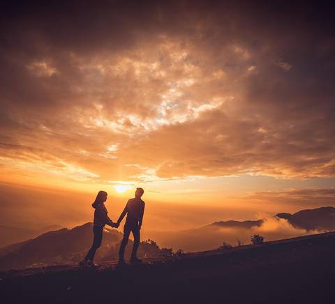 Una pareja se toma de las manos frente a un hermoso atardecer en la montaña.