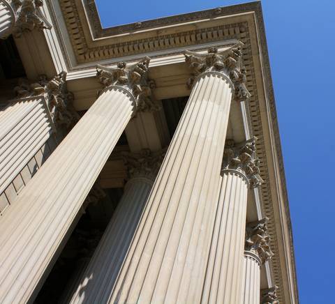 La imagen muestra columnas clásicas de un edificio bajo un cielo azul claro.