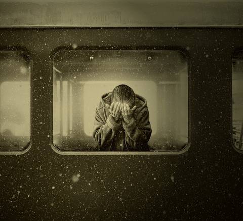 Una persona está sentada detrás de una ventana de tren, con la cabeza entre las manos, mientras cae nieve en el exterior.