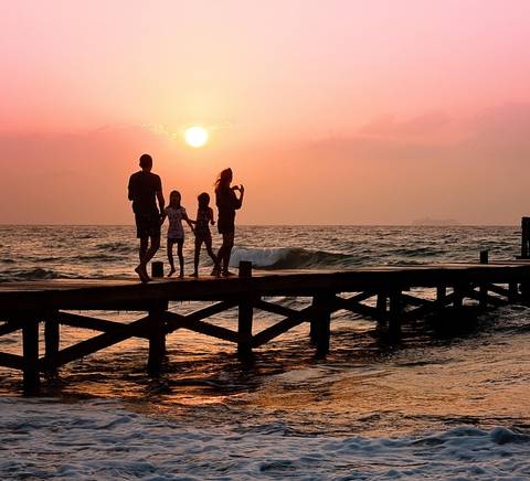 Una familia pasea por un muelle al atardecer, con el sol poniéndose en el horizonte.