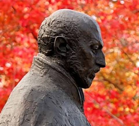 Una escultura de perfil rodeada de hojas de otoño en colores rojos.