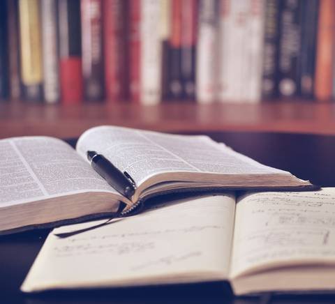 Una imagen que muestra libros abiertos sobre una mesa, con un bolígrafo descansando sobre ellos.