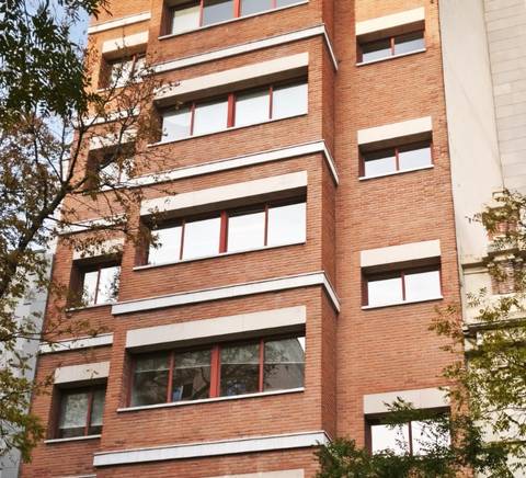 Edificio de ladrillo con ventanas enmarcadas en color blanco y árboles alrededor.